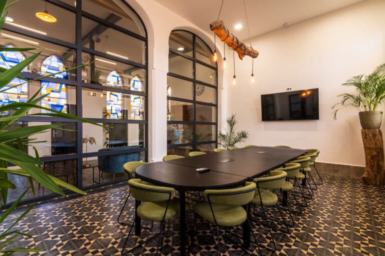 Intérieur d'une salle de réunion moderne avec une grande table noire, des chaises vertes, des fenêtres à vitraux et un écran de télévision.