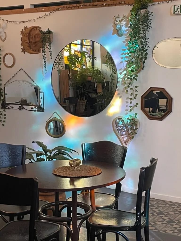 Un coin de café décoré avec des miroirs, des plantes, et une table ronde, baigné de lumière colorée.