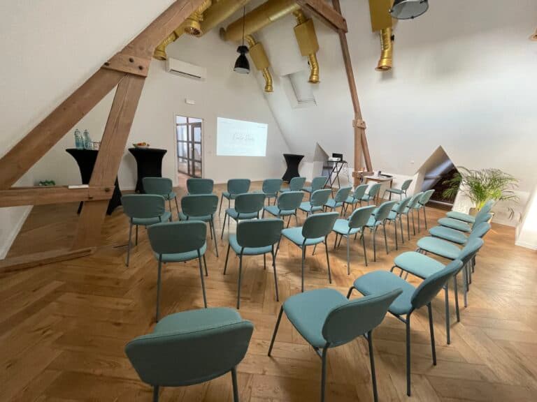 Une salle de réunion moderne avec des chaises bleues disposées en cercle, un écran de projection et des éléments de décoration en bois et en métal.