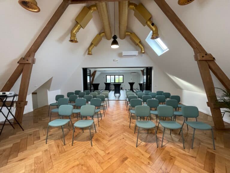 Une salle de réunion moderne avec des chaises vertes disposées en rangées et des poutres en bois apparentes.